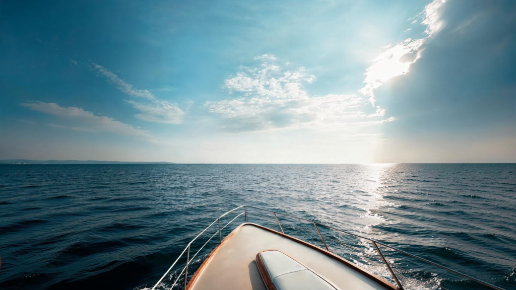The bow of a vessel heading across open ocean toward a bright horizon