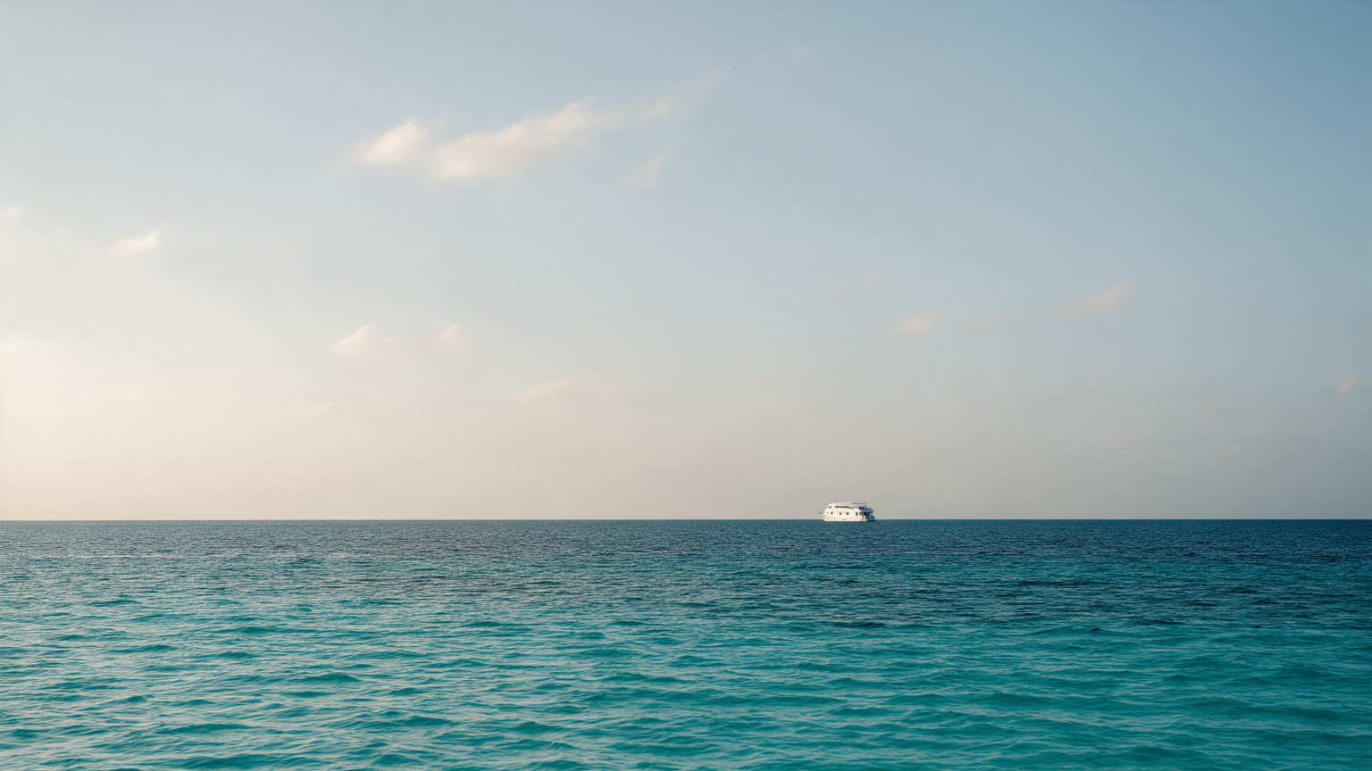 A white liveaboard vessel on a calm turquoise Indian Ocean horizon in the Maldives